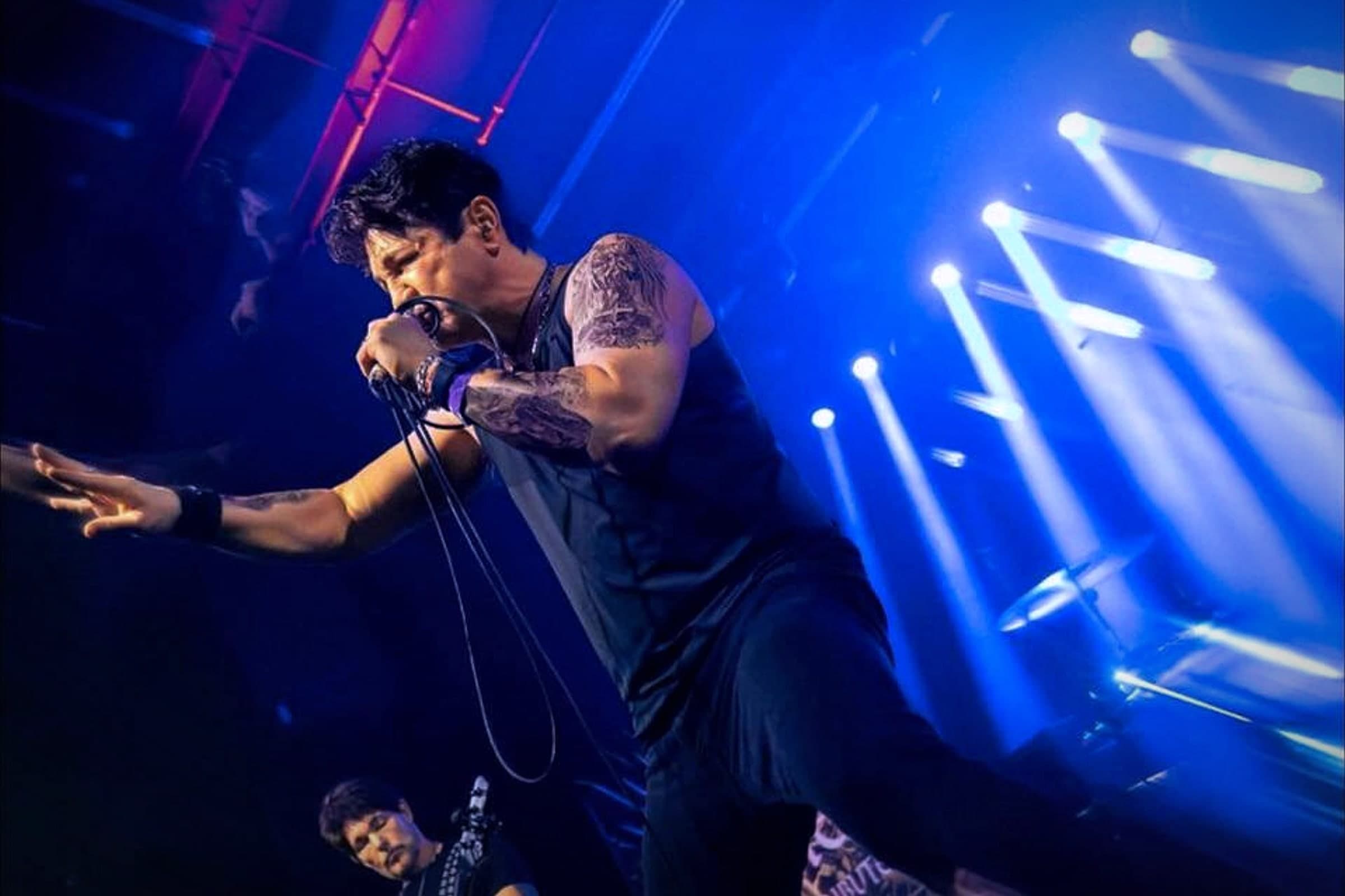 Steven Traikovich of Higher Creed Tribute singing under blue stage lights, with a bandmate playing behind him